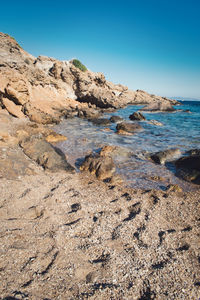 Rocks on beach against clear blue sky