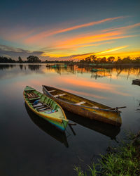 Boat moored in lake against sky during sunset