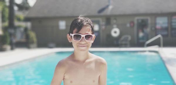 Portrait of shirtless boy wearing sunglasses while standing against swimming pool