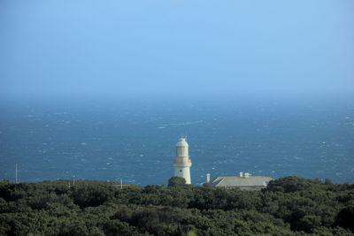 Lighthouse by sea against clear sky