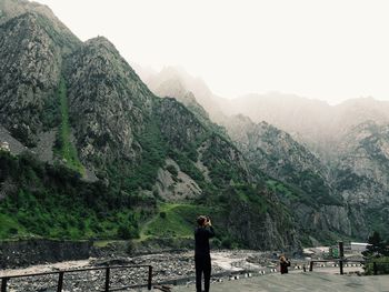 Man clicking photograph of mountains against clear sky