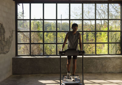 Full length profile shot of a young man running on a treadmill at home.