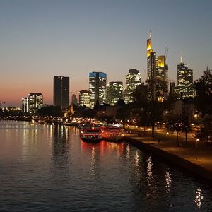 Illuminated buildings by river against sky in city