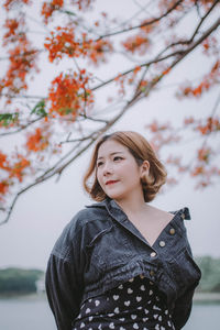 Young woman looking away while standing against tree