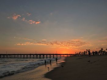 Silhouette people on beach against sky during sunset