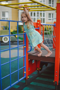 Girl hanging on a horizontal bar in the playground in summer