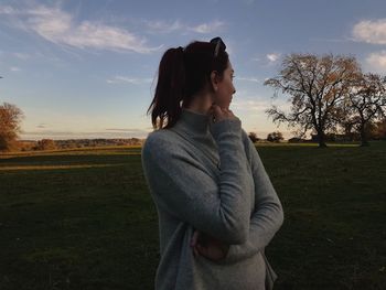 Young woman looking away while standing on land against sky