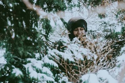 Smiling woman amidst snow covered tree in forest