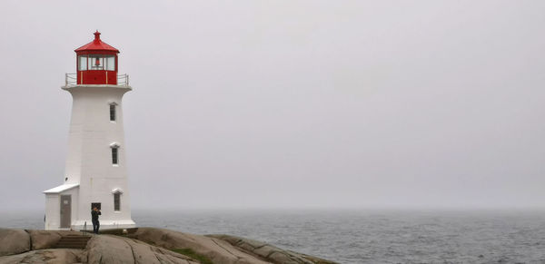 Lighthouse amidst sea and buildings against sky