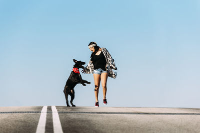 Woman with dog and skateboard against clear blue sky