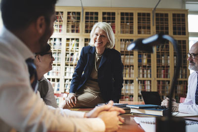 Happy senior lawyer sitting on table during meeting in library