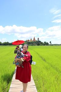 Portrait of mid adult woman with pug carrying red umbrella standing on landscape