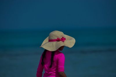 Rear view of girl wearing sun hat at beach against sky