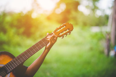 Cropped hand of person playing guitar over field