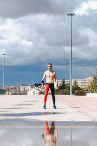 Portrait of shirtless man reflecting on puddle while standing at street