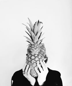 Man holding pineapple in front of face against white background