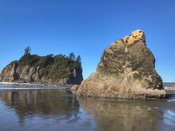 Rock formations in sea against clear blue sky