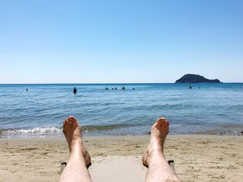 Low section of man at beach against clear blue sky