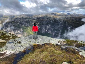 Rear view of man standing on rock mountain against sky