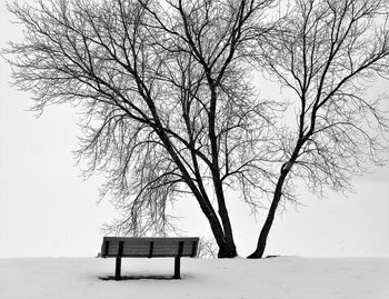 Empty bench on snow covered land against sky