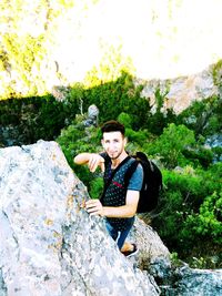 Portrait of young man sitting on rock against trees