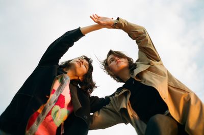 Low angle view of women holding hands against sky