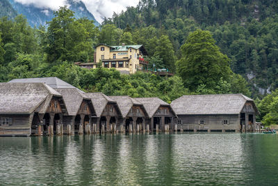 House and trees by lake against buildings