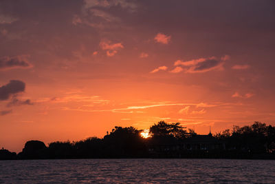 Silhouette trees by lake against romantic sky at sunset