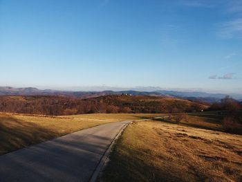 Road leading towards mountains against clear blue sky