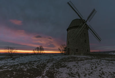 Traditional windmill on field against sky during sunset