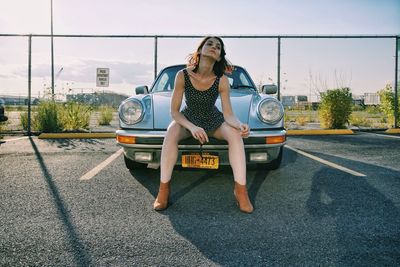 Young woman sitting on car against sky