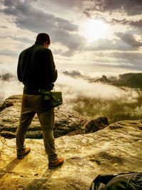 Rear view of man standing on field against sky during sunset