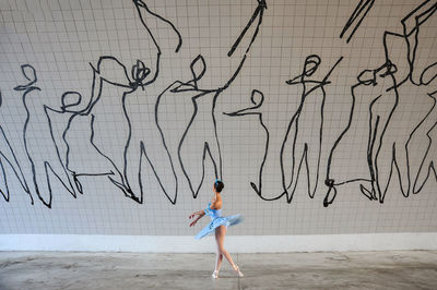 Side view of woman dancing against graffiti wall
