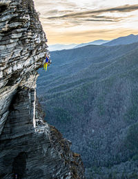 Man hanging over rock on mountain against sky