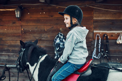Little smiling girl learning horseback riding. 5-6 years old equestrian in helmet having fun riding