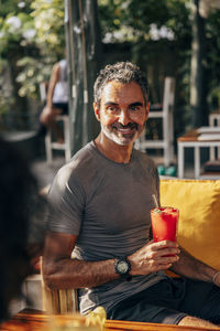 Smiling mature man holding juice glass while sitting at wellness resort