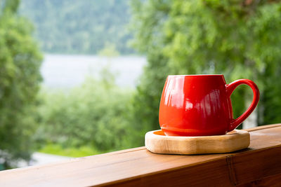 Morning coffee in garden. red mug on wooden board against blurred nature.