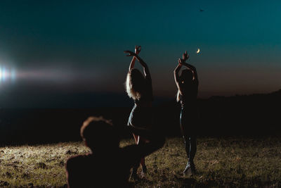 Silhouette women with arms raised against sky during dusk