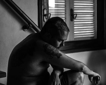 Side view of thoughtful shirtless man sitting by window