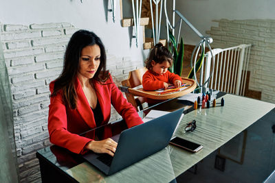 Young executive woman working from home while taking care of her young daughter