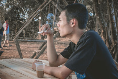 Side view of young man smoking cigarette while sitting at park