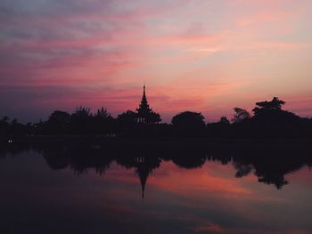 Reflection of silhouette trees and temple in lake during sunset