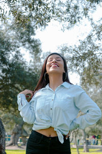 Smiling young woman standing against trees