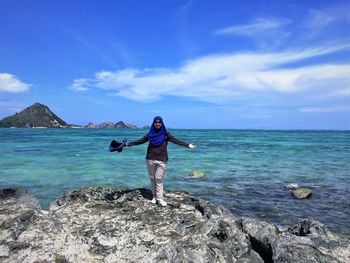 Full length of woman standing on rock at beach against sky