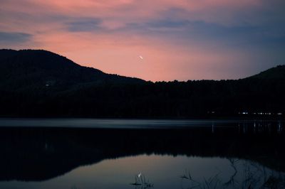 Scenic view of lake by silhouette mountains against sky at sunset