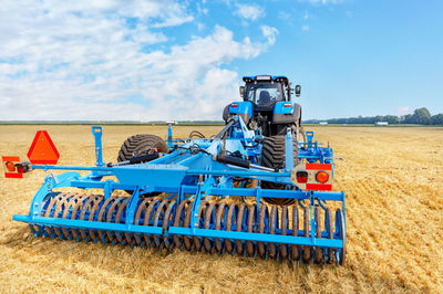 A powerful universal blue harrow on an agricultural tractor against the background of yellow field.