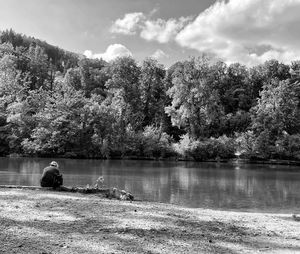 Man sitting by lake against sky