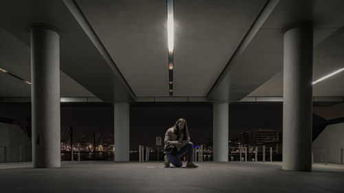 Portrait of girl kneeling in illuminated parking lot at night