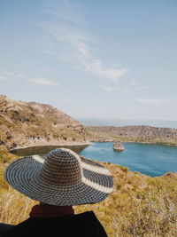 Rear view of woman in hat by sea against sky