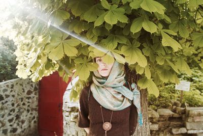 Portrait of young woman standing below tree